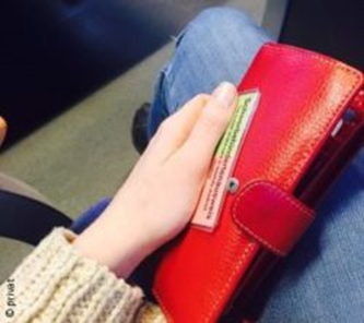 Leonie Höpfner sitzt im Zug und sie hält ihre Geldtasche und ihren
Schwerbehindertenausweis in der Hand.