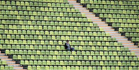 Auf diesem Foto ist ein Mensch in einer weiten leeren
                  Zuschauertribüne abgebildet.