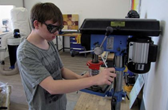 Ein Junge steht in der Holzwerkstatt und arbeitet mit einer
                  Maschine.
