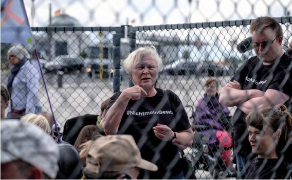 Foto von mehreren Personen in einem Käfig mit schwarzen T-Shirts mit der
                     Aufschrift "#NichtmeinGesetz"