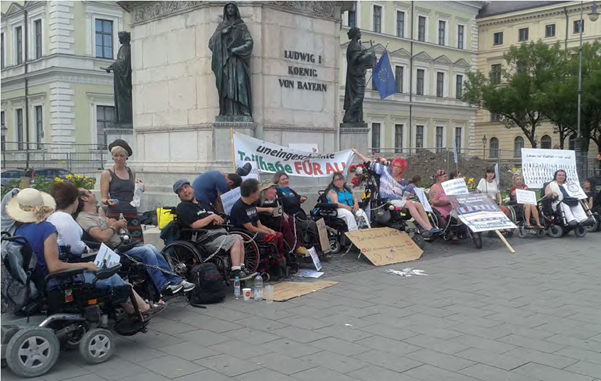 Foto der Protestkundgebung in München mit mehreren Personen in Rollstühlen
                  und Plakaten.