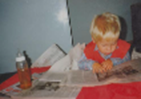 Foto eines kleinen Jungen der an einem Tisch sitzt 