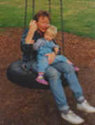 Foto eines Mannes der mit einem Kind auf dem Arm auf der Schaukel
                     sitzt